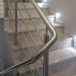 Schody wyłożone marmurem z nowoczesną metalową barierką, oświetlenie punktowe w ścianie.