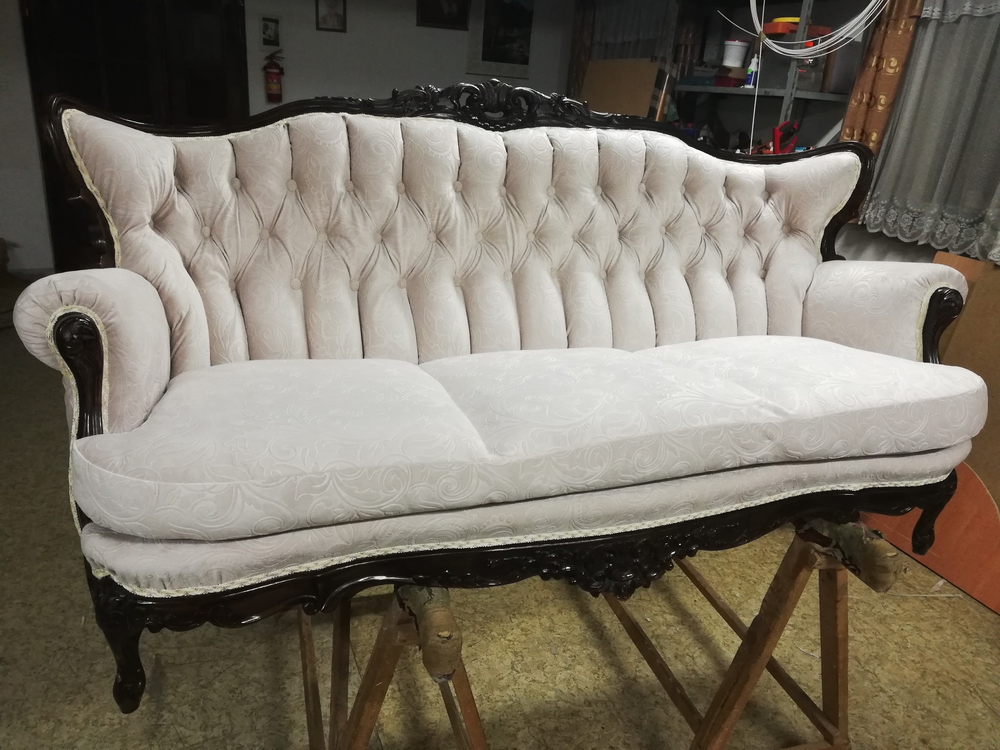 Odrestaurowana sofa w stylu vintage z kremową tapicerką w delikatny wzór, umieszczona na drewnianych kozłach w warsztacie.