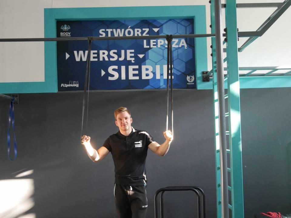 Trener personalny we Wrocławiu prezentuje ćwiczenia na kółkach gimnastycznych w siłowni, w tle hasło 'Stwórz lepszą wersję siebie'.