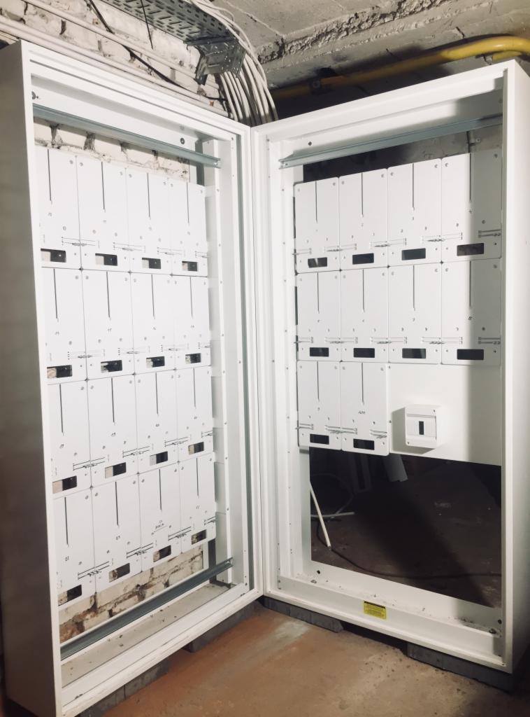 Otwarta szafa telekomunikacyjna z widocznymi modułami i okablowaniem wewnątrz, zamontowana na ceglanej ścianie, z widocznymi elementami instalacji w tle.