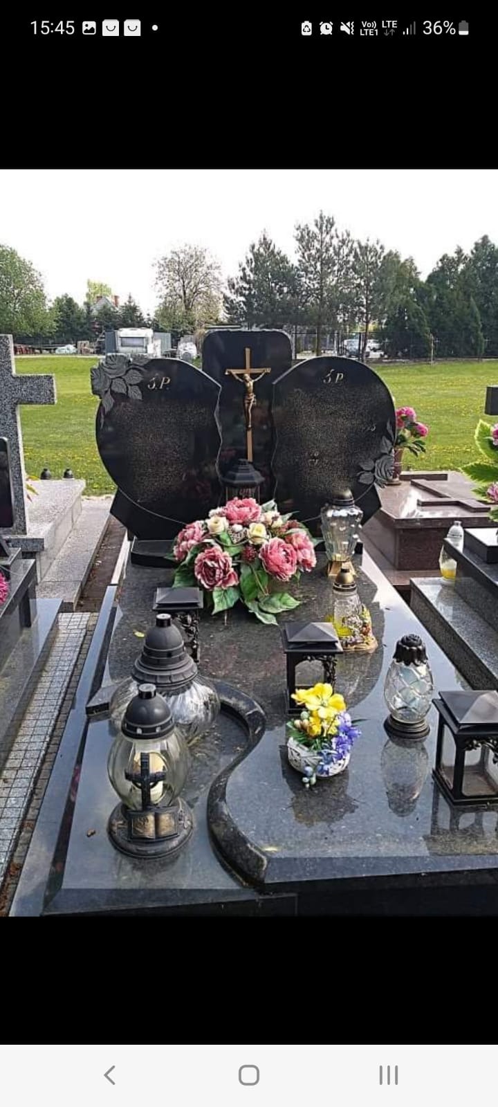 Czarny, granitowy nagrobek z krzyżem i kwiatami, ozdobiony lampionami na cmentarzu, widok z przodu.