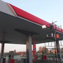 Mobilna Myjnia Mycie Pełną Parą - Pracownik na rusztowaniu czyści z zewnątrz zadaszenie stacji benzynowej Orlen, używając wiadra i szczotki, widoczne dystrybutory paliwa i cennik.