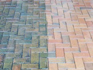 Częściowo wyczyszczona kostka brukowa ułożona we wzór jodełki; widoczna wyraźna różnica w kolorze między czystą, jasną częścią a zabrudzoną, ciemniejszą.