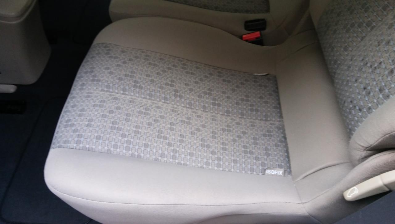 Szare samochodowe siedzenie z wzorem w małe kwadraty, widoczny fragment pasów bezpieczeństwa i oznaczenie ISOFIX.