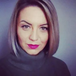 Portret kobiety z blond bobem, mocnym makijażem ust i zielonym golfem na tle szarej ściany.