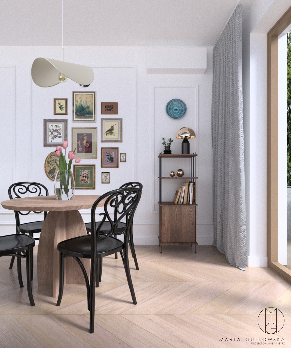 Jadalnia w jasnych barwach z okrągłym, drewnianym stołem i czarnymi krzesłami w stylu wiedeńskim. Na ścianie galeria obrazków i półka z książkami. Parkiet ułożony w jodełkę.