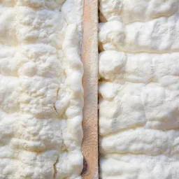 Świeżo nałożona, puszysta, biała pianka izolacyjna wypełniająca przestrzeń między drewnianymi belkami konstrukcyjnymi, widoczne nierówności i struktura pianki.