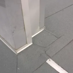 Szary dach pokryty papą, z widocznym kominem obłożonym blachą, oraz uszczelnieniem przy podstawie komina.