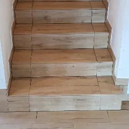 Wykończone schody z płytek imitujących drewno, z widocznymi fugami i listwami przypodłogowymi, prowadzące w górę.