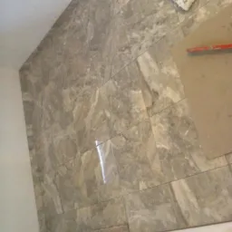 Układanie szarych, marmurkowych płytek na podłodze, widoczna karta do rozprowadzania kleju i gąbka do czyszczenia fug.