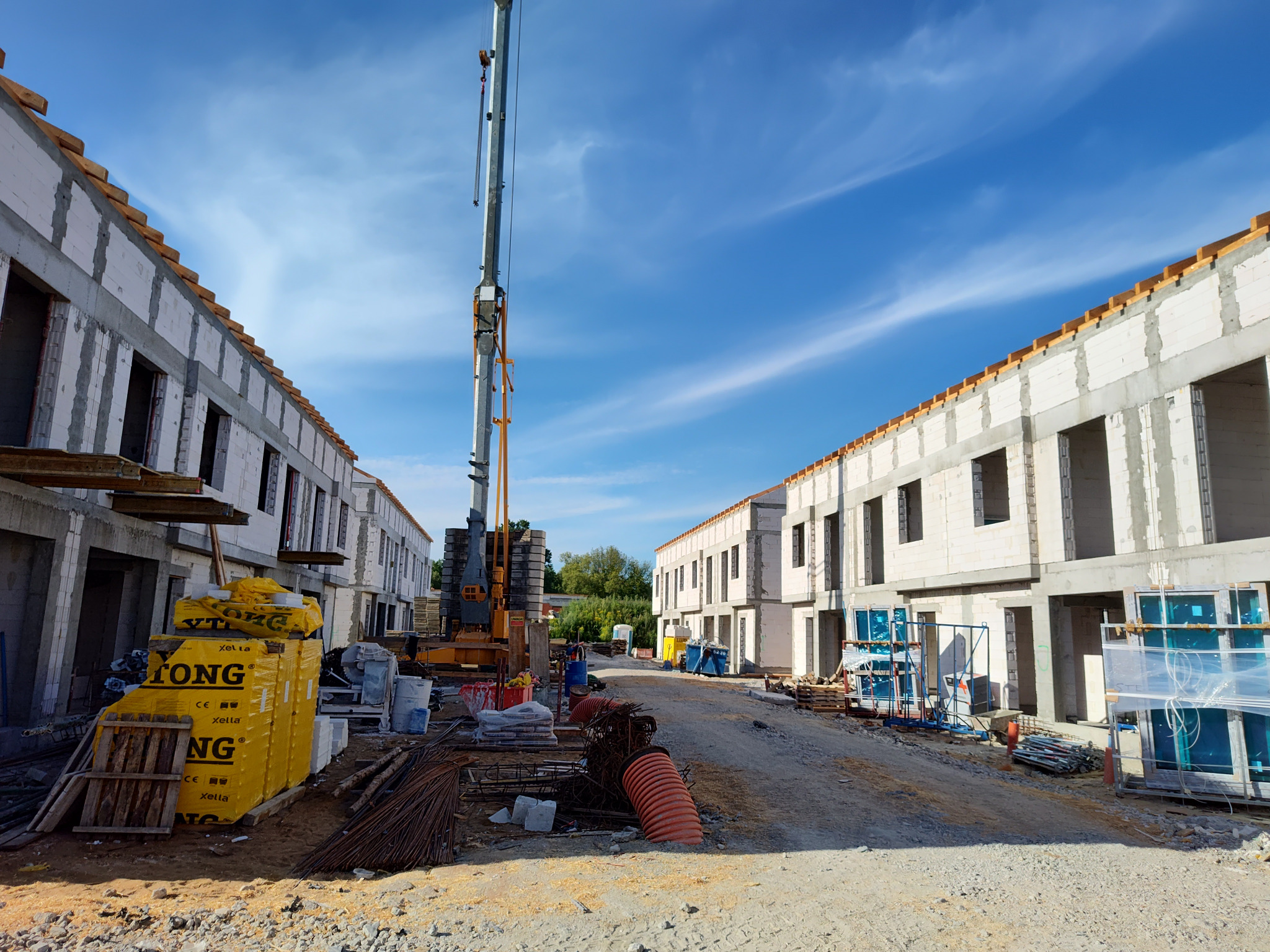 Budowa szeregu domów w stanie surowym otwartym. Widoczne bloki Ytong, dźwig budowlany i materiały budowlane. Błękitne niebo w tle. Góraszka, ul. Południowa.