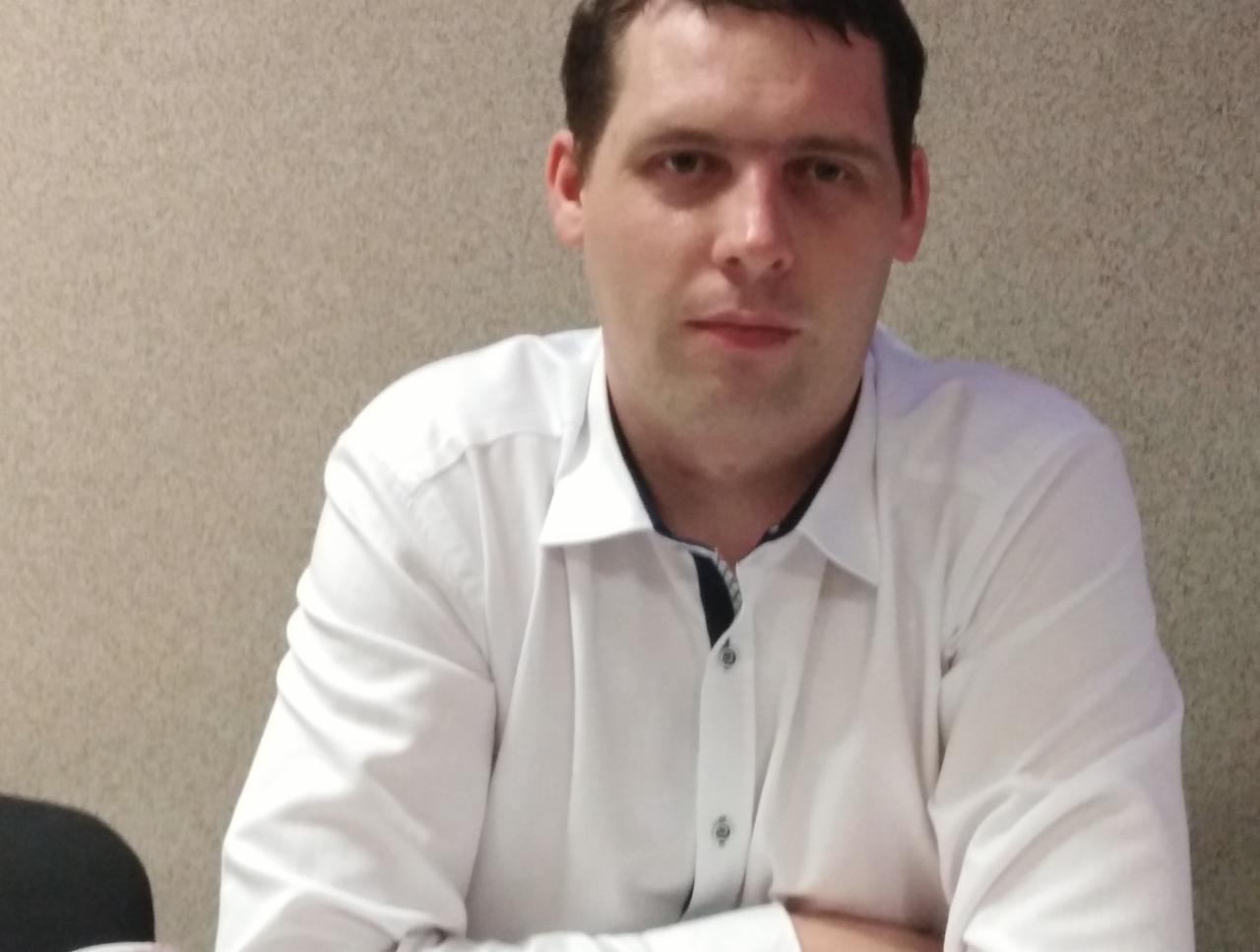Portret mężczyzny w białej koszuli z podwiniętymi rękawami na tle beżowej ściany. Zdjęcie profilowe 'Głażewski'.