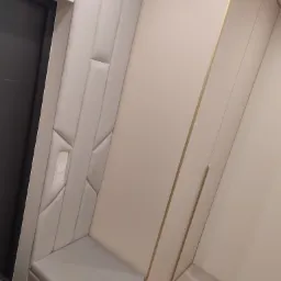 Tapicerowany panel ścienny z geometrycznym wzorem i wbudowanym siedziskiem w przedpokoju, obok szafy wnękowej z subtelnymi złotymi akcentami.