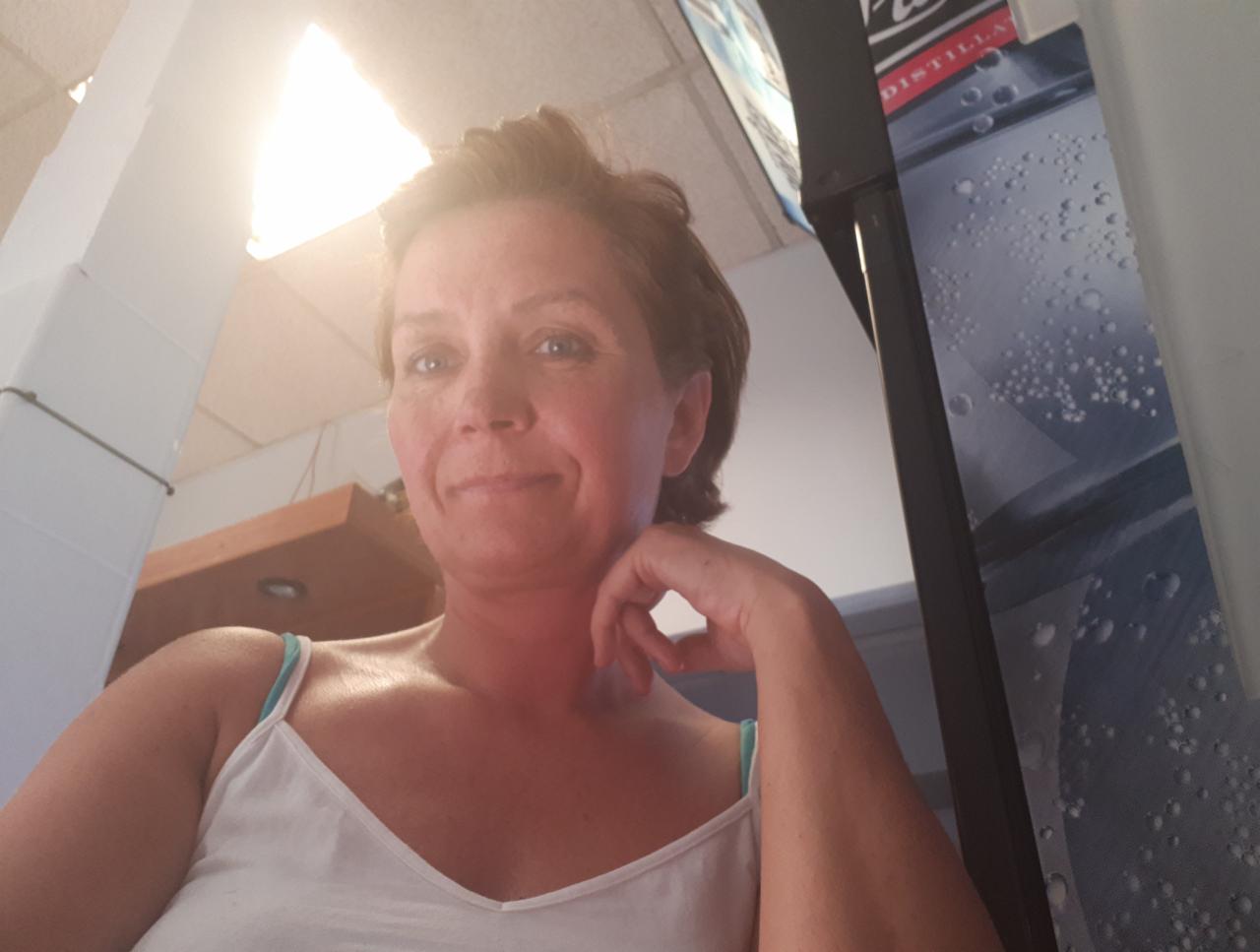 Portret kobiety z ręką pod brodą, w tle widoczny fragment biura z oświetleniem i elementami wyposażenia.