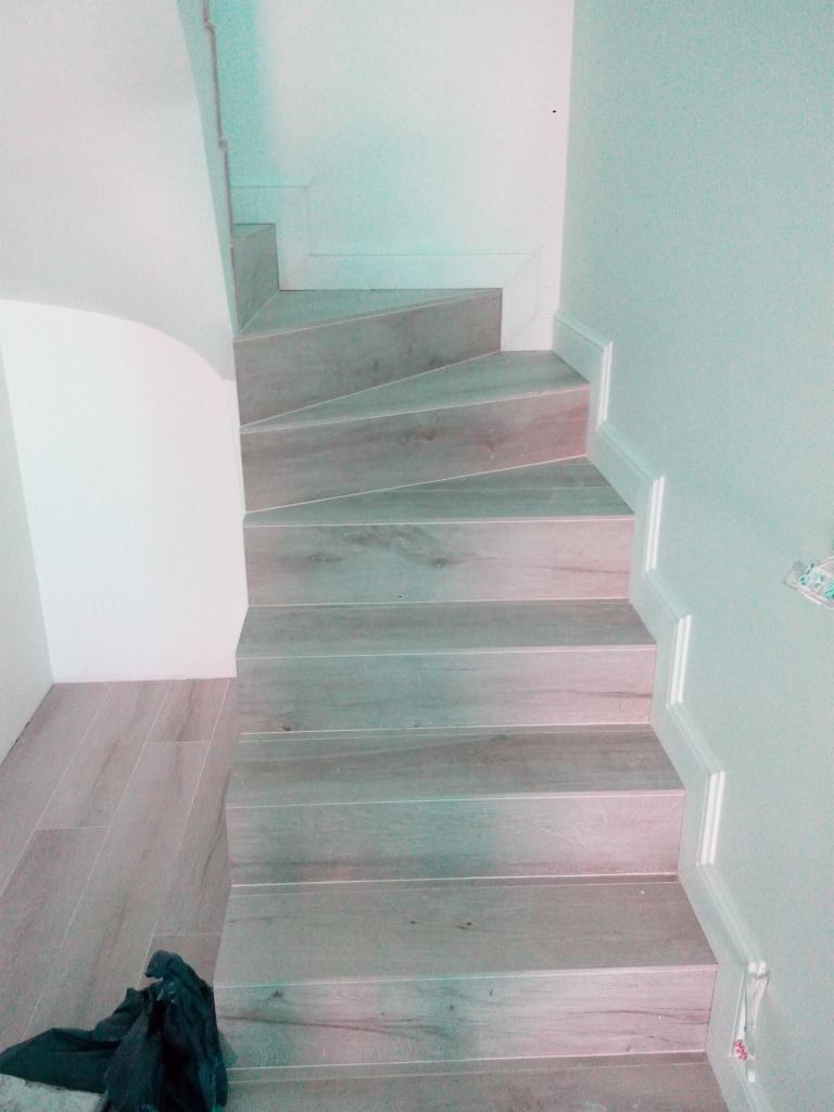 Wykończone schody wewnętrzne z płytek imitujących drewno, białe listwy przypodłogowe, widoczny fragment podłogi i robocze ubranie.