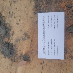 Wizytówka firmy ogólnobudowlanej leżąca na zabrudzonej powierzchni z resztkami zaprawy, prezentująca zakres usług: budowa domów od podstaw, ocieplanie budynków, wykończenia wnętrz, ogrodzenia...