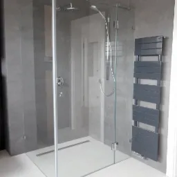 Nowoczesna kabina prysznicowa ze szklanymi ścianami i deszczownicą, zamontowana w łazience wykończonej szarymi płytkami, z widocznym grzejnikiem drabinkowym.
