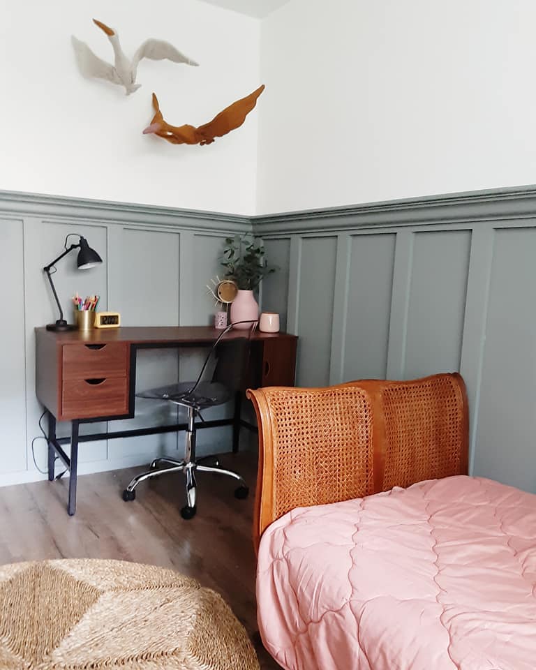 Pokój dziecięcy z drewnianym biurkiem, krzesłem na kółkach, łóżkiem z plecionym zagłówkiem i dekoracjami dinozaurów na ścianie.