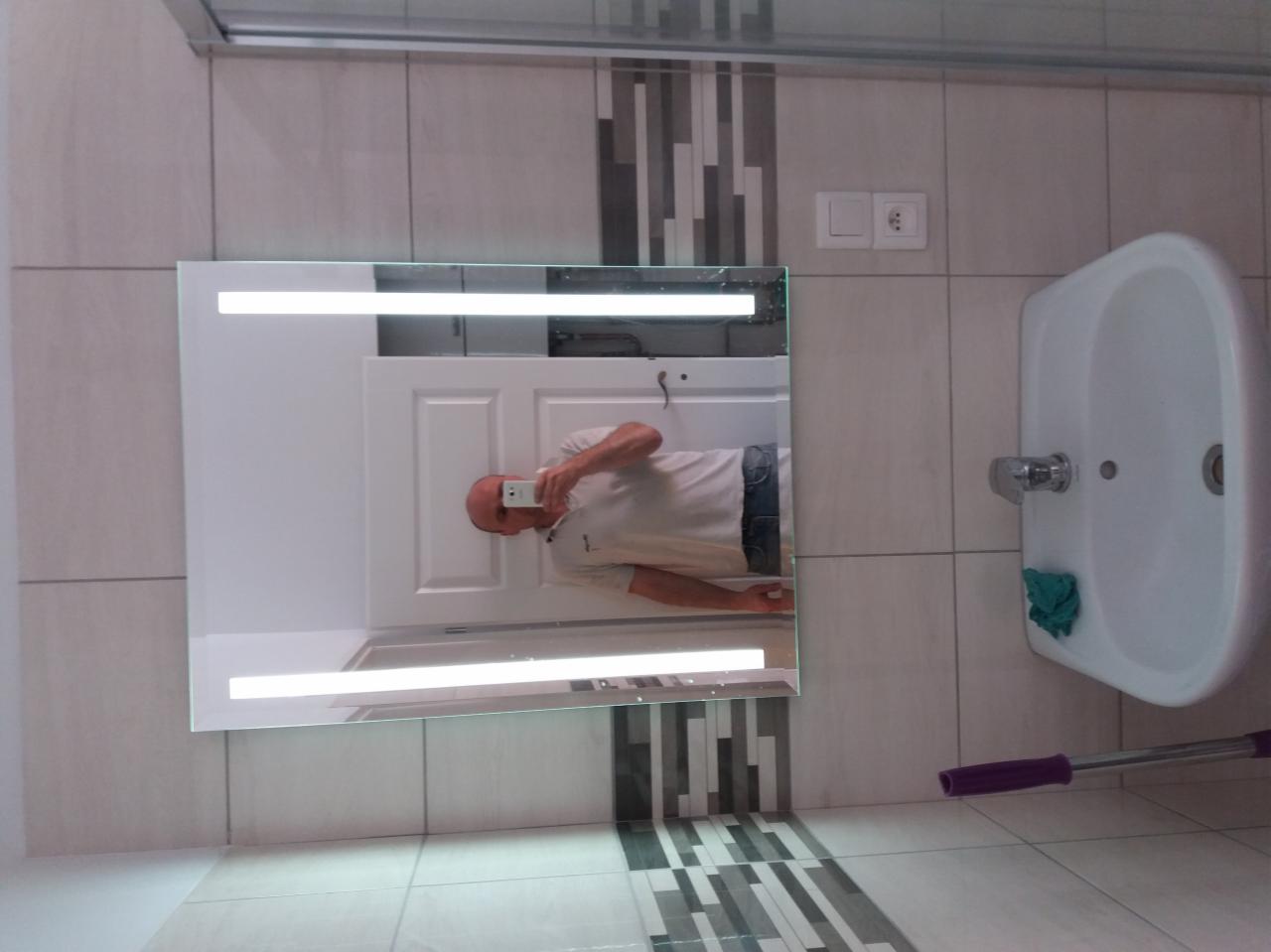 Nowoczesna łazienka z podświetlanym lustrem, białą umywalką i mozaiką w odcieniach szarości, widoczny fragment mopa.