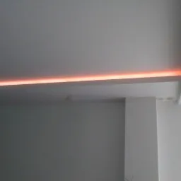 Nowoczesne oświetlenie LED w suficie podwieszanym, emitujące ciepłe, pomarańczowe światło, widoczne także dwa okrągłe reflektory wbudowane w sufit.