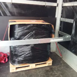 Paczka owinięta czarną folią stretch zabezpieczona pasami wewnątrz przestrzeni ładunkowej pojazdu na palecie euro.