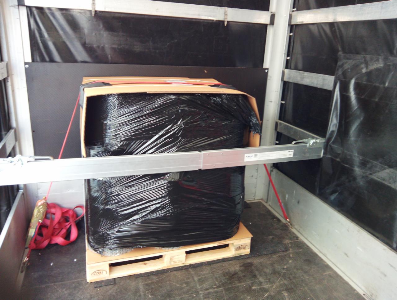 Paczka owinięta czarną folią stretch zabezpieczona pasami wewnątrz przestrzeni ładunkowej pojazdu na palecie euro.