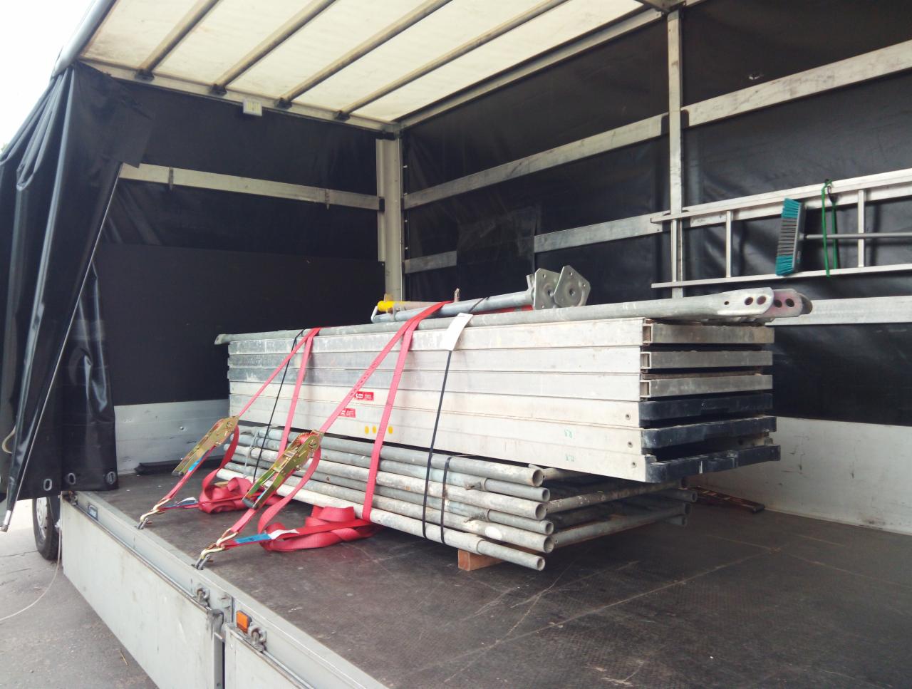 Wnętrze skrzyni ładunkowej busa z zabezpieczonym ładunkiem rusztowania, spiętym czerwonymi pasami transportowymi.