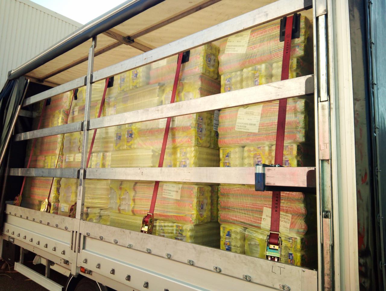 Wnętrze naczepy ciężarówki wypełnione paletami z towarem zabezpieczonym czerwonymi pasami transportowymi.