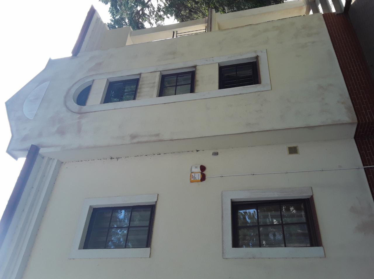 Dwupiętrowy budynek z kremową elewacją przed i po myciu, widoczne różnice w czystości powierzchni, okna z ciemnymi ramami i nietypowy owalny element architektoniczny w górnej części.