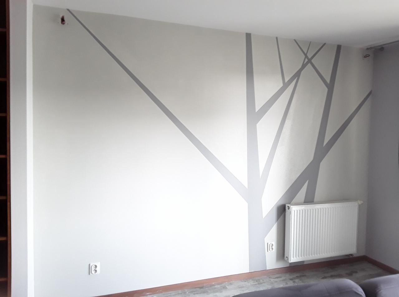 Ściana w pokoju z ręcznie malowanym, szarym wzorem drzewa bez liści, obok grzejnik.