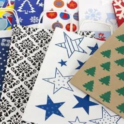 Zestaw papierowych toreb prezentowych z różnorodnymi wzorami świątecznymi: choinki, gwiazdy, bombki, płatki śniegu, w kolorach czerwieni, błękitu, zieleni i bieli.