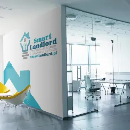 Wnętrze biura z logo firmy zarządzającej najmem, widoczne dwa żółte krzesła i szklana ściana oddzielająca przestrzeń biurową.