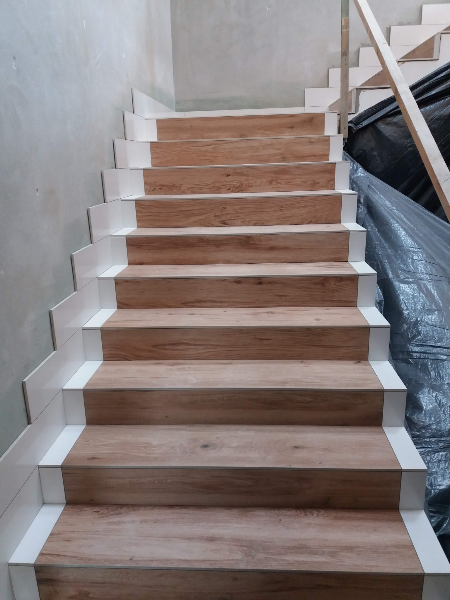Schody wyłożone płytkami imitującymi drewno, z białymi listwami wykończeniowymi, widok z dołu na górę.
