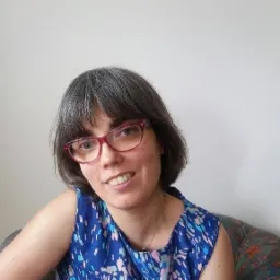 Portret uśmiechniętej kobiety w okularach z granatową bluzką, prawdopodobnie tłumaczki.