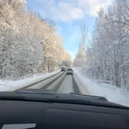 Zimowa droga widziana z wnętrza samochodu, drzewa oblepione śniegiem po obu stronach, dwa samochody jadące w oddali.