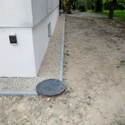 Izolacja fundamentów domu z widocznym drenażem z kamyków i studzienką rewizyjną.