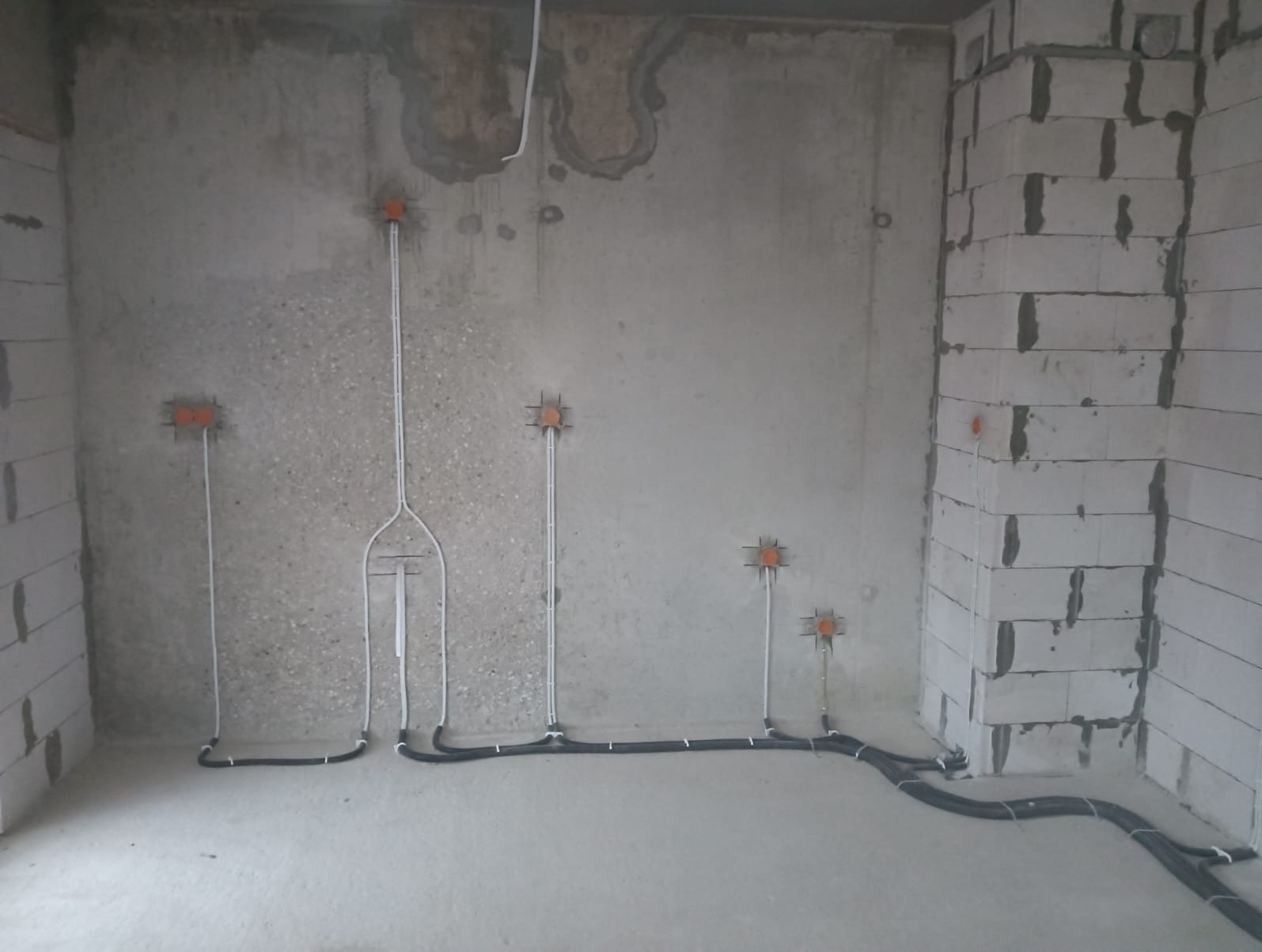 Surowy stan: kable elektryczne w peszlach prowadzone po ścianie z betonu komórkowego, puszki instalacyjne osadzone w ścianie, widoczne etapy przygotowania do montażu osprzętu.