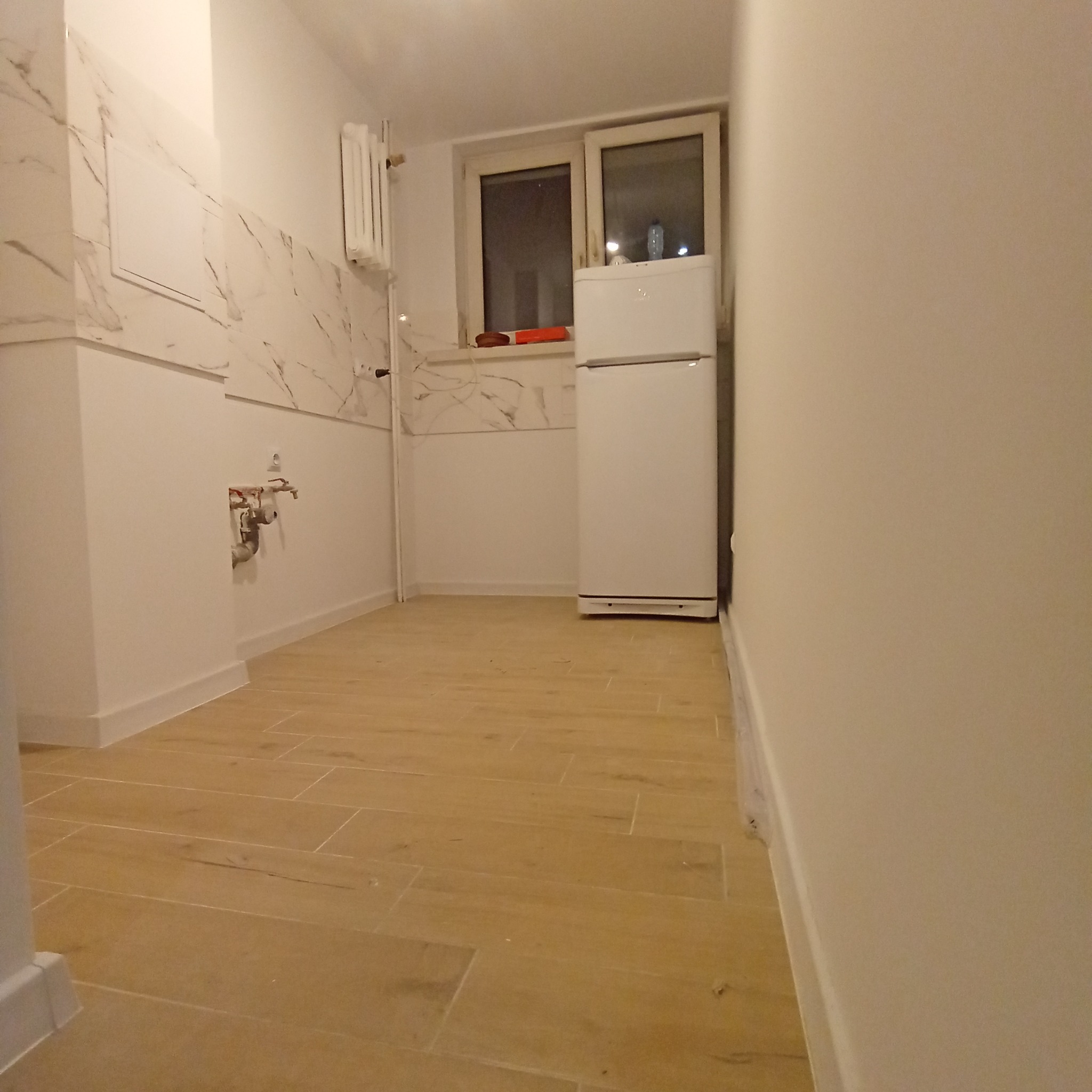 Jasna kuchnia po remoncie z drewnopodobną podłogą, marmurowymi płytkami na ścianie i białą lodówką.