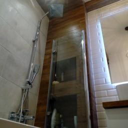 Gres-Bud - Wykończona łazienka z kabiną prysznicową z pojedynczym szklanym panelem, deszczownicą i baterią natryskową, z beżowymi płytkami ściennymi i imitacją drewna na suficie i ścianie, oraz białymi...