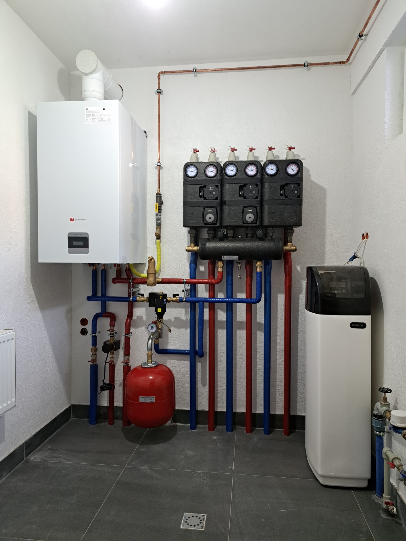 Nowoczesna kotłownia z białym kotłem gazowym Saunier Duval, rozdzielaczem grzewczym z manometrami, czerwonym zbiornikiem wyrównawczym i zmiękczaczem wody Supreme Logic, rury miedziane i instalacja...