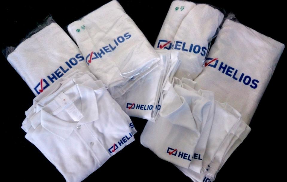 Stos ubrań i ręczników z nadrukowanym logo firmy Helios, część z nich zapakowana w foliowe torby.