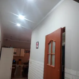 Korytarz po remoncie z pomalowanymi ścianami na szaro i zamontowaną drewnianą ościeżnicą drzwiową z szybami, widok na kuchnię w tle.