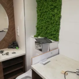 Montaż podtynkowej spłuczki WC z zieloną ścianą z mchu w nowoczesnej łazience w trakcie remontu.