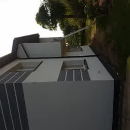 Nowoczesny dom jednorodzinny z jasnoszarą elewacją i ciemnoszarymi, pionowymi pasami dekoracyjnymi; widoczna aluminiowa drabina oparta o ścianę.