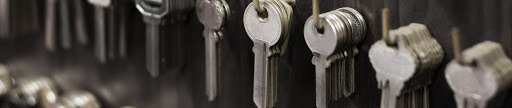 Rząd srebrnych kluczy zawieszonych na metalowych kółkach, widoczne różne kształty i wzory nacięć, tło ciemne, lekko rozmyte.