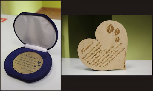 Dwa drewniane upominki z wygrawerowanymi dedykacjami, jeden w kształcie serca z odciśniętymi ustami i tekstem, drugi w okrągłym pudełku z niebieskiego aksamitu z grawerem na złotym tle.