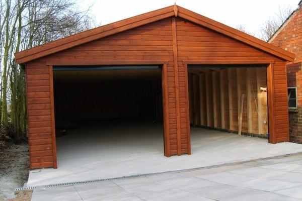 Dwustanowiskowy garaż z drewna, z widoczną konstrukcją szkieletową w jednej części i wykończoną elewacją w drugiej, na betonowej wylewce.