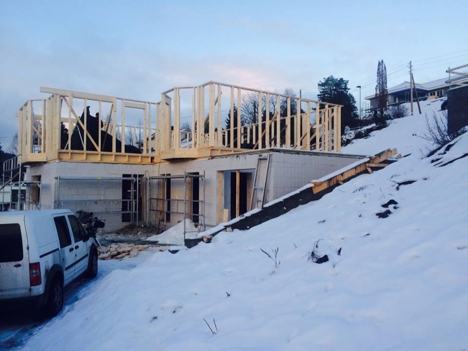 Budowa domu w zimowej scenerii: surowy stan, ściany z bloczków, drewniana konstrukcja szkieletowa drugiego piętra, biały van na pierwszym planie.