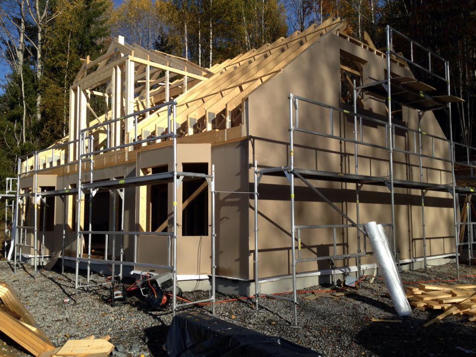 Budowa domu jednorodzinnego w trakcie montażu więźby dachowej i elewacji, widoczne rusztowania, materiały budowlane i narzędzia na placu budowy.