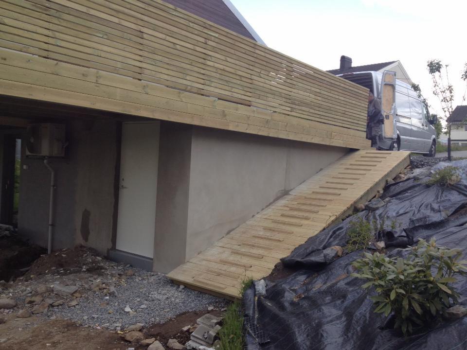 Drewniany taras w trakcie budowy w Zawierciu, z widoczną rampą dostępową i częściowo wykończoną elewacją budynku.